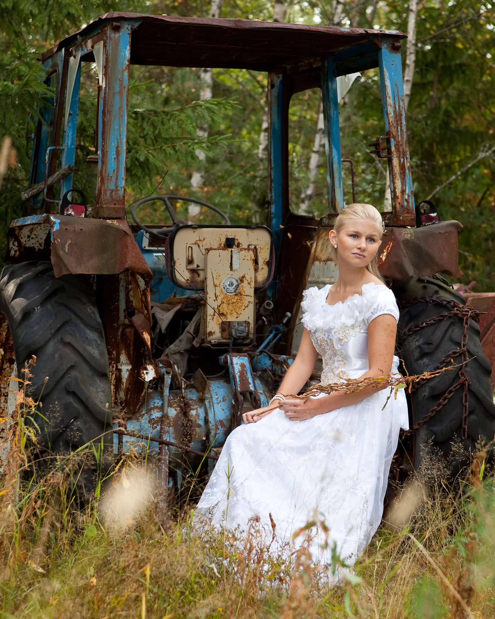 Ruth in white gown beside rustic tractor in countryside