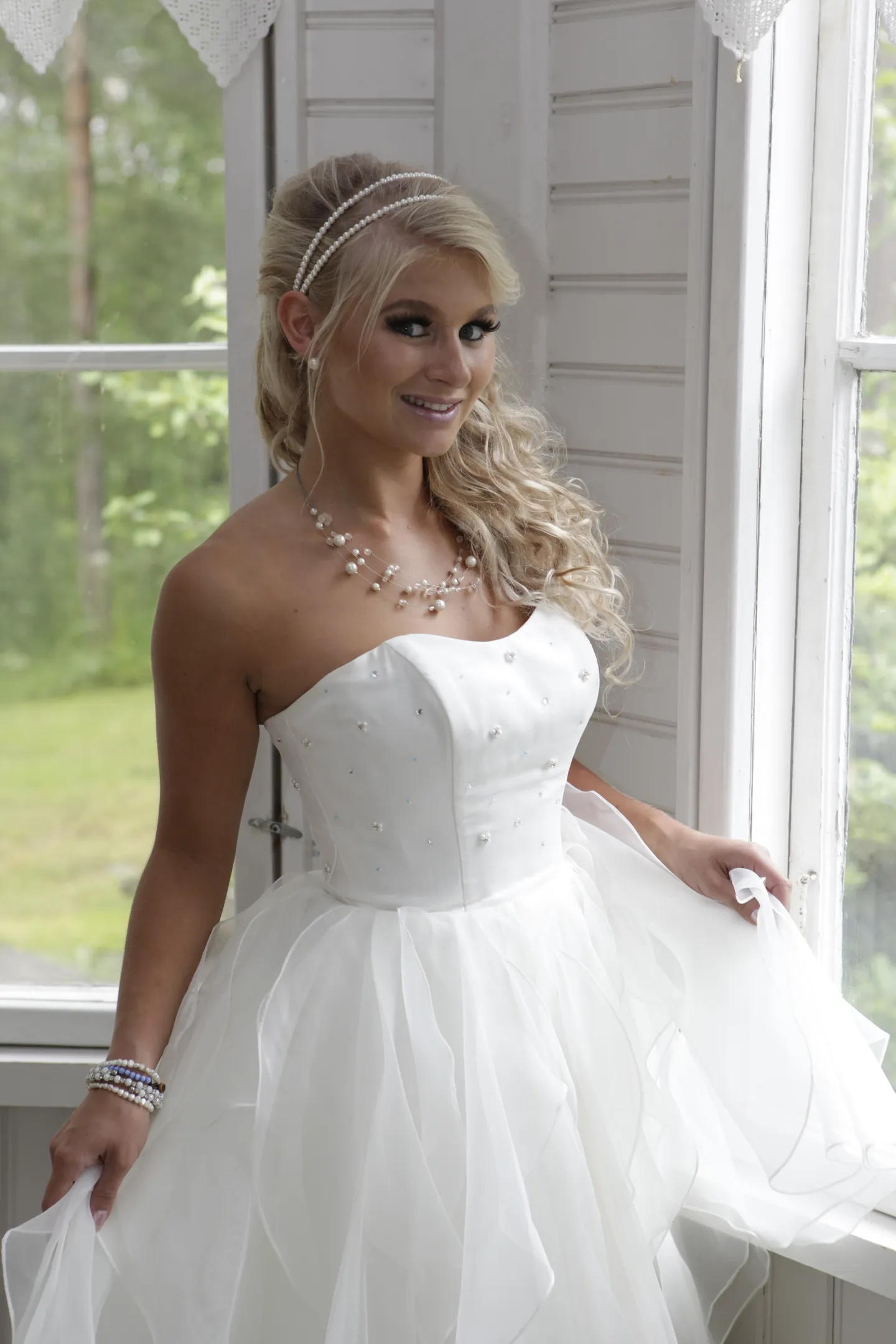 Ruth smiling in white tulle dress by sunlit veranda window