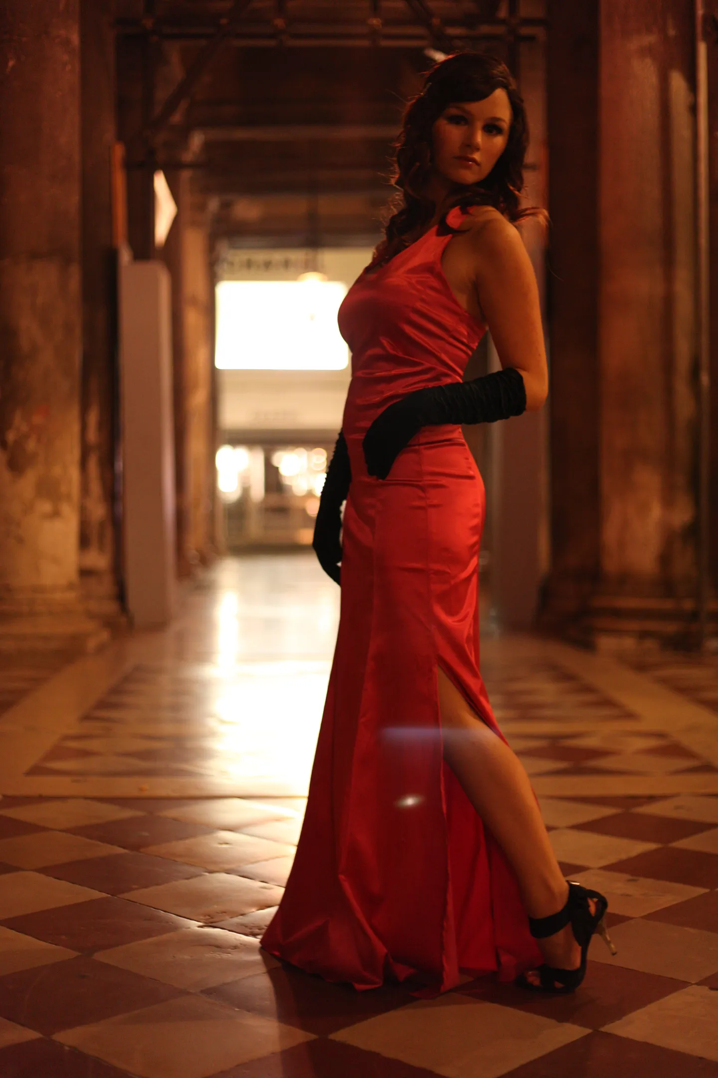 Ruth in red satin gown and black gloves in grand hallway, film noir