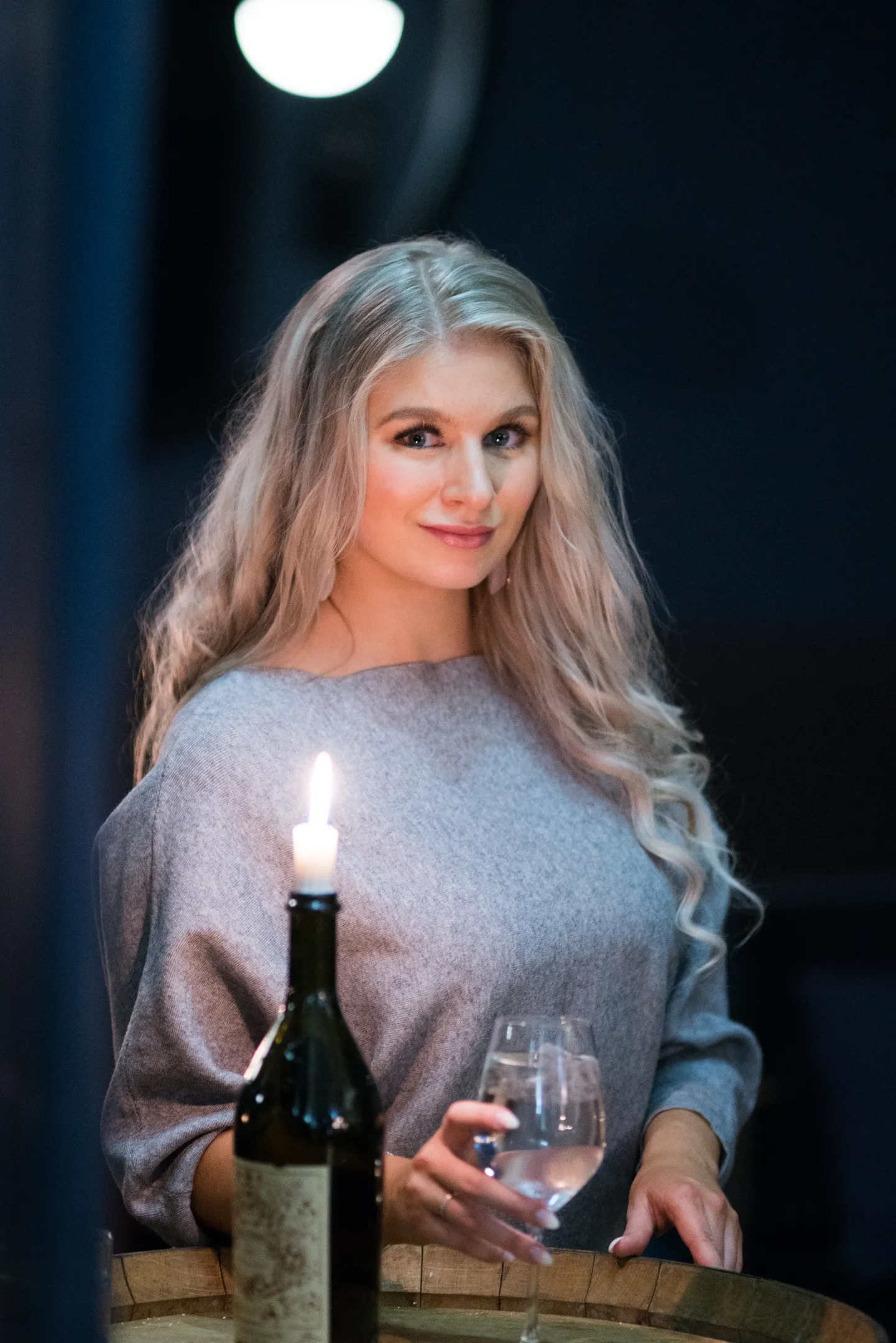 Ruth holding wine glass by candlelight in dark cellar setting