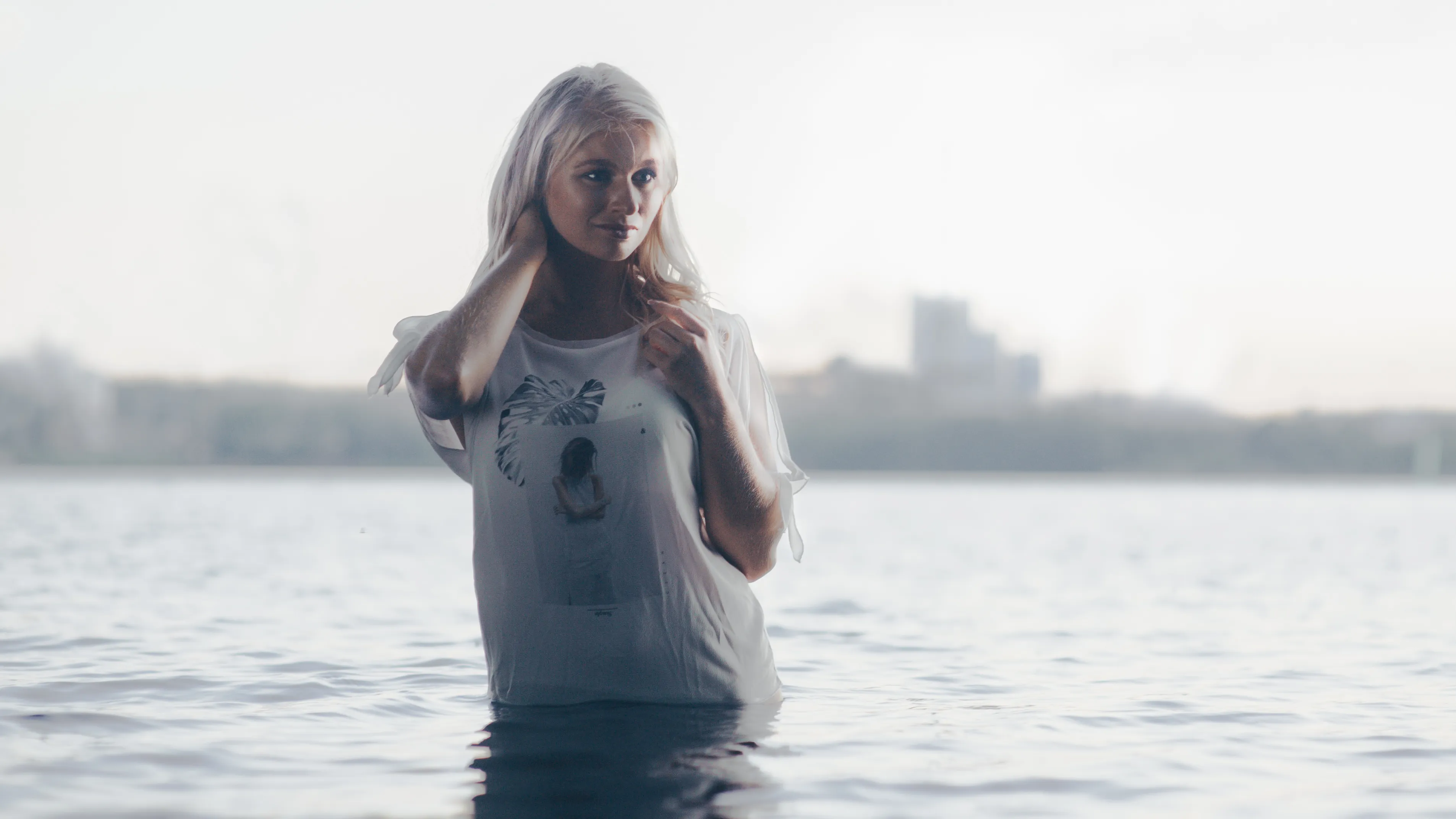 Ruth standing in lake at golden hour in white tee, wide shot