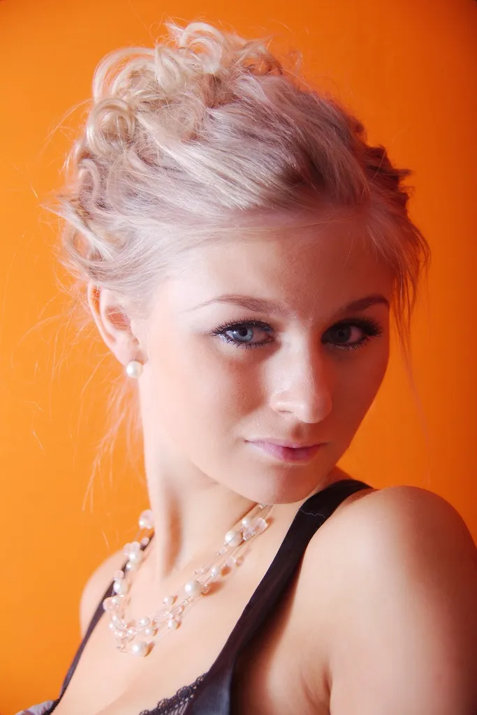 Ruth in pearl necklace and updo, tight beauty headshot on orange