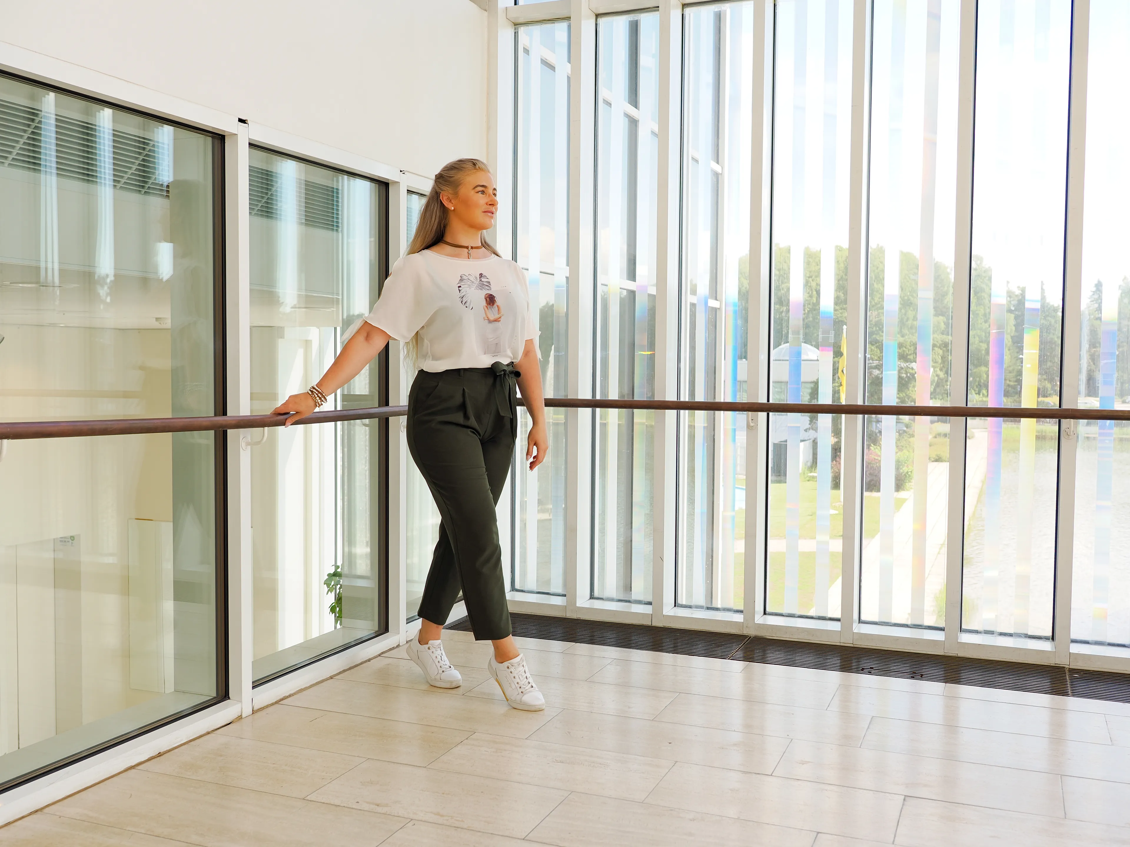 Ruth in casual outfit leaning on railing in bright modern building