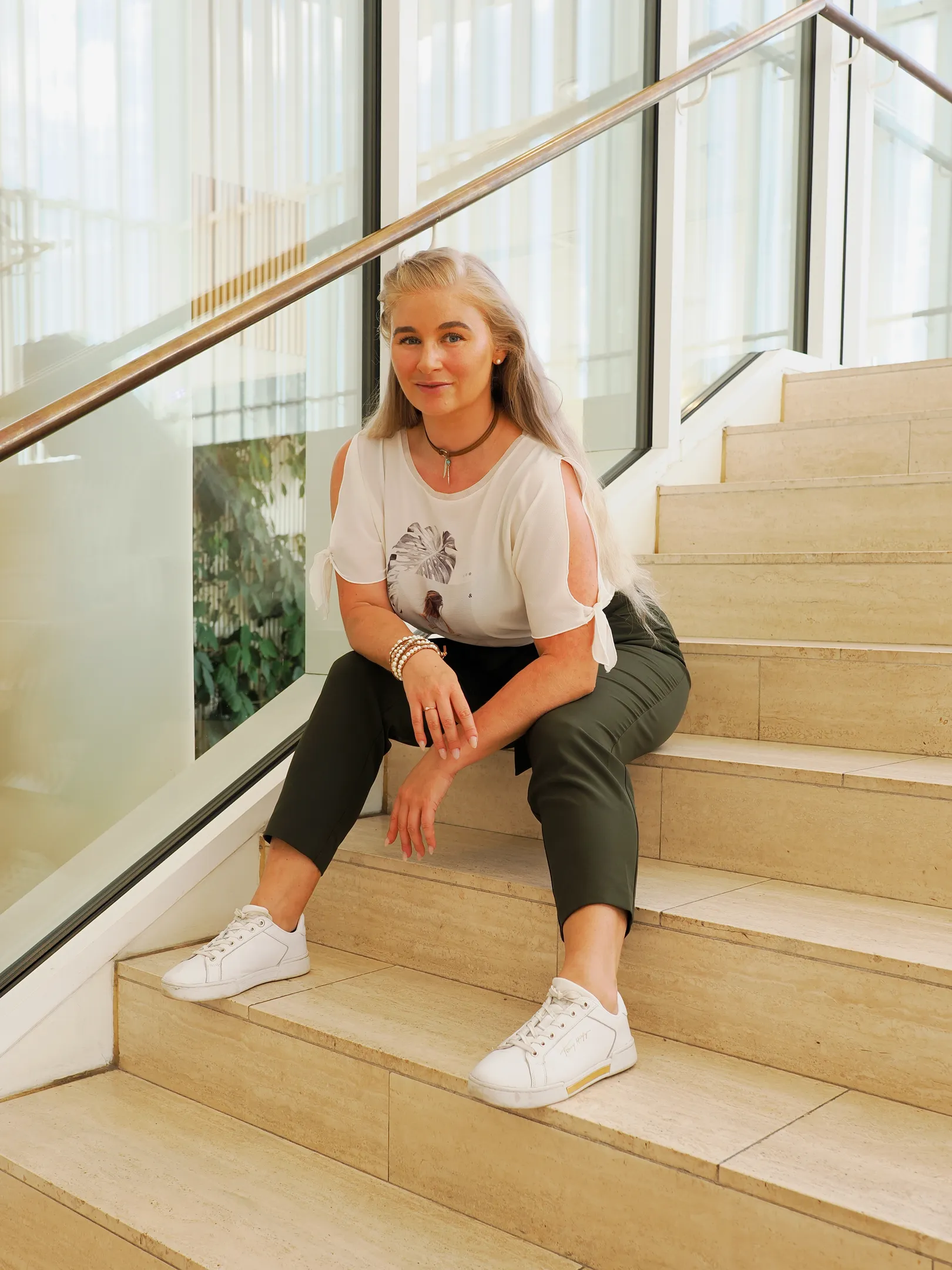 Ruth sitting on modern staircase in casual white top and dark pants