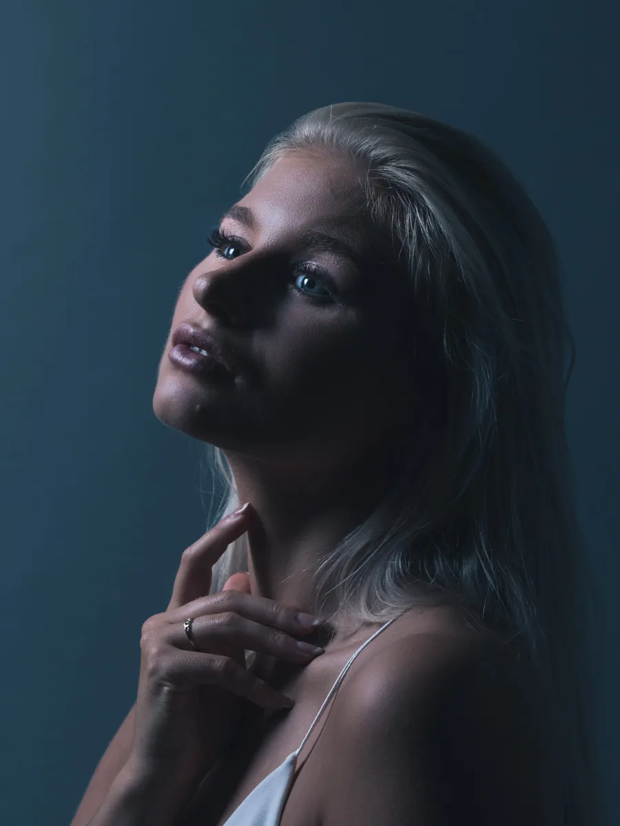 Ruth in moody blue-lit portrait with white camisole and windswept hair