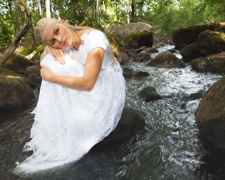Ruth in white dress sitting in forest stream, dreamy fairy tale