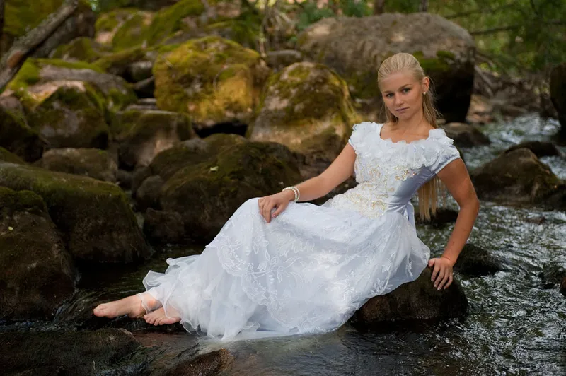 Ruth in white dress seated on rocks in flowing stream