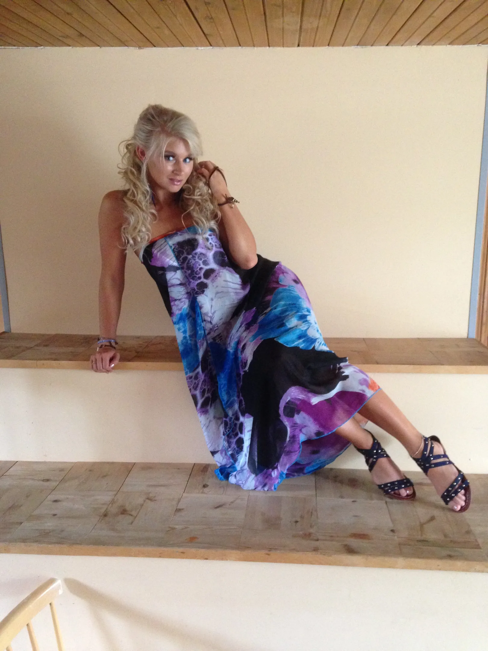 Ruth in colorful strapless maxi dress reclining on wooden bench