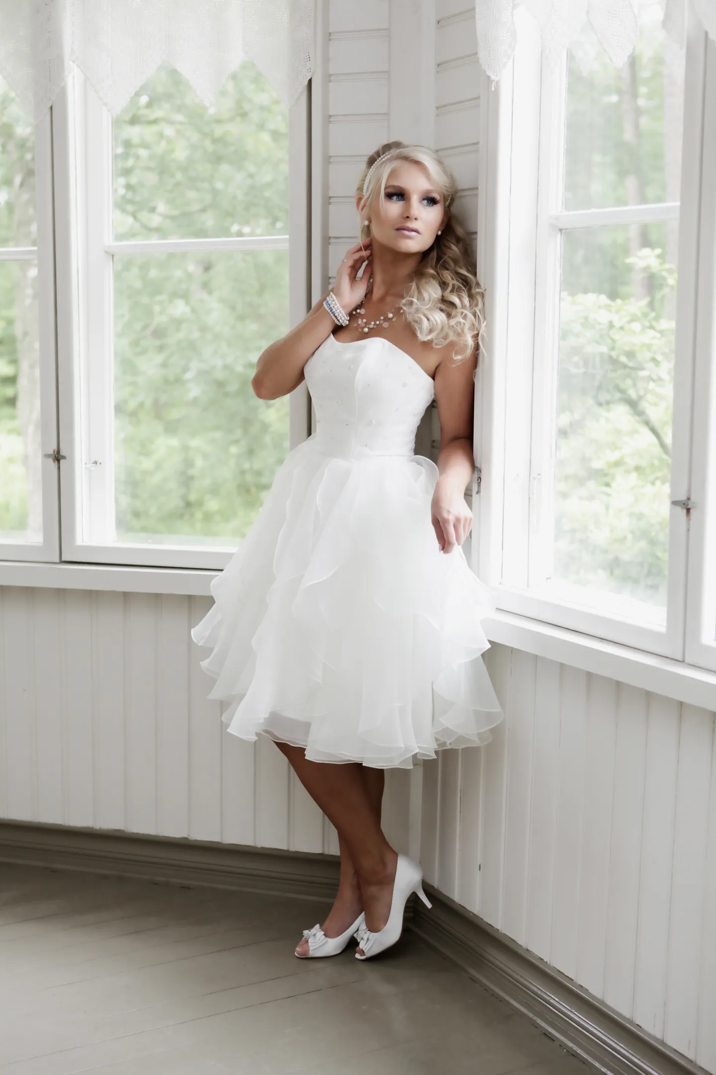 Ruth in white cocktail dress by window in bright veranda