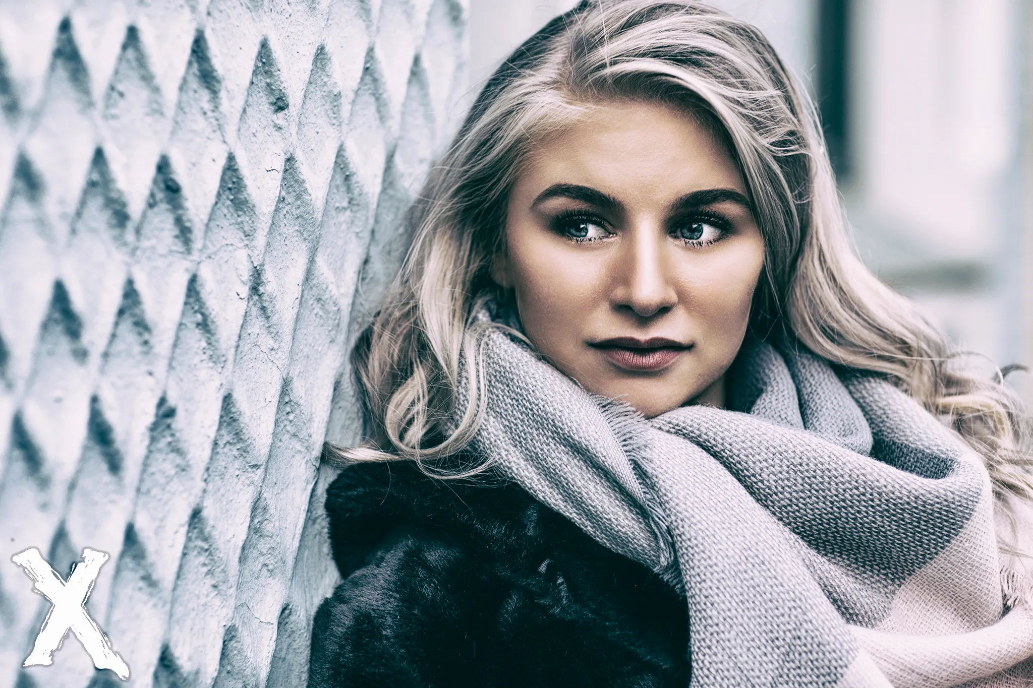 Ruth in fur coat and scarf leaning against textured wall, winter