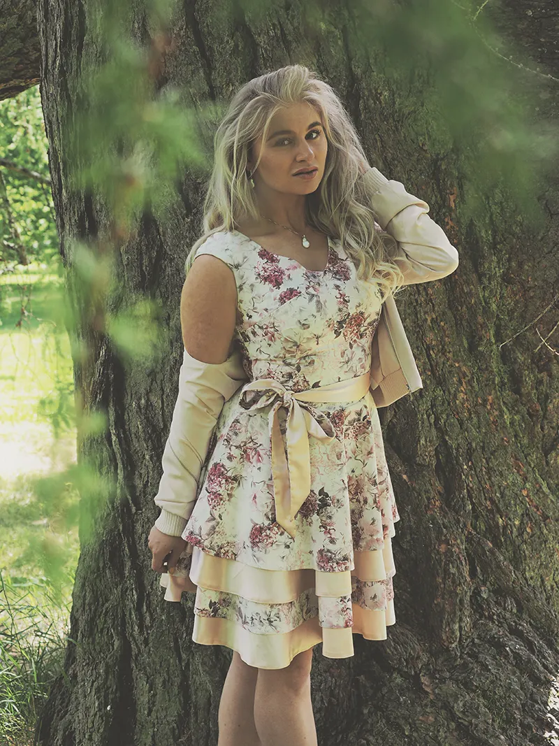 Ruth in floral dress leaning against oak tree, soft outdoor light