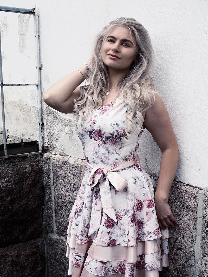 Ruth in floral dress leaning against stone wall outdoors