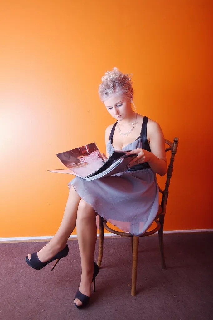 Ruth reading a magazine in heels against an orange wall